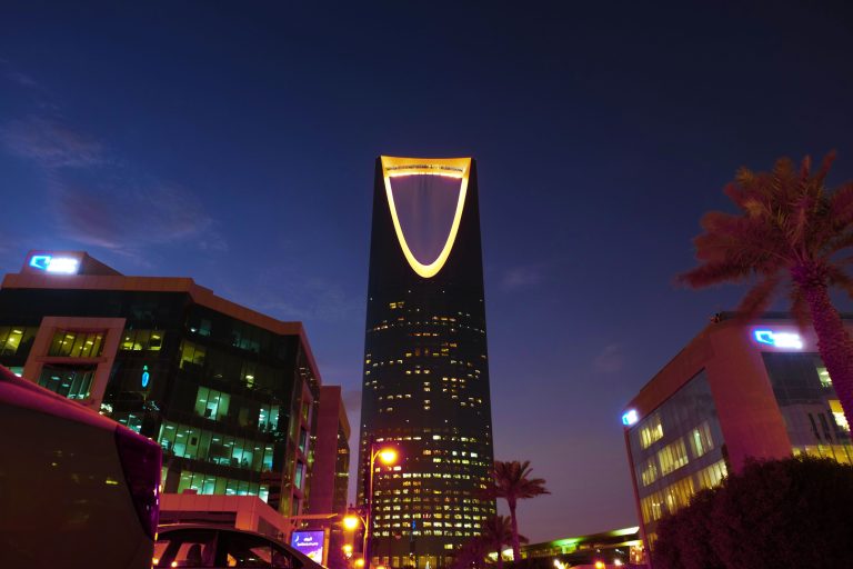 Illuminated Kingdom Centre Tower rising in Riyadh's urban landscape at twilight.